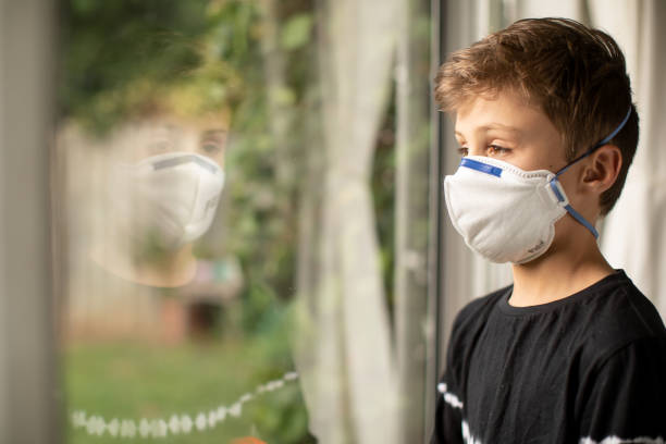 istock Boy in mask looking out window 1215232265