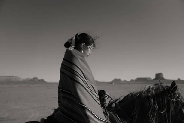 ein junger navajo in traditioneller kleidung, reiten ihr pferd, schwarz und weiß still - monument valley navajo mesa monument valley tribal park stock-fotos und bilder