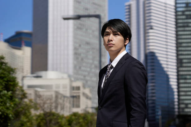A Japanese businessman stands in an office district with a serious expression on his face
