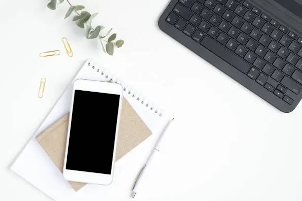 Photo of Female workspace with laptop computer keyboard, smartphone with blank screen mockup, paper notepad and notebook. Stylish home office desk table concept