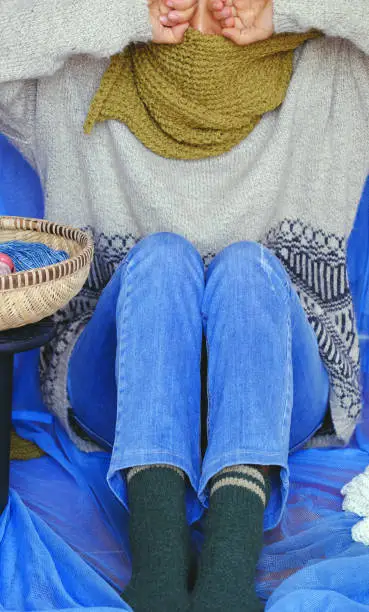 Woman wear blue jeans, white woolen sweater, sock and moss green wool scarf sit with blue background, knitted handmade product to make warm for winter as hobby in free time
