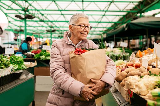 Old woman carrying a paper bag full of fruits and vegetables, shopping for groceries and smiling