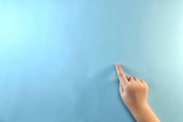 Hand gesture of a child pointing a finger at an empty surface of the background.