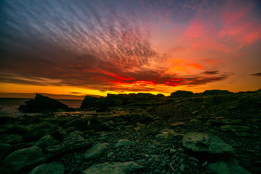 Dramatic night sky on fire off the rocky coastal landscape at Cape Palliser at sunset