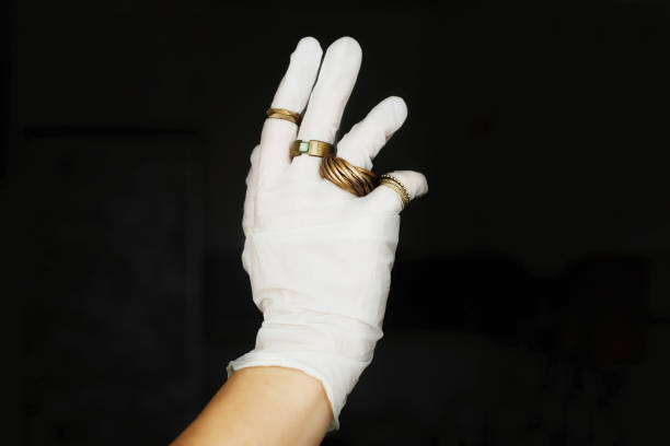 moda i kwarantanna. ręka w białej rękawiczce medycznej z nowoczesnymi pierścieniami na palcach na czarnym tle.  ochrona skóry, zapobieganie wirusom w dobrym stylu. pozytywne wibracje podczas epidemii. - bronze rubber plastic metal zdjęcia i obrazy z banku zdjęć