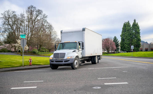 istock Small compact semi truck with cube box trailer transporting commercial cargo driving on the street of urban city in spring time with blooming trees 1215266601