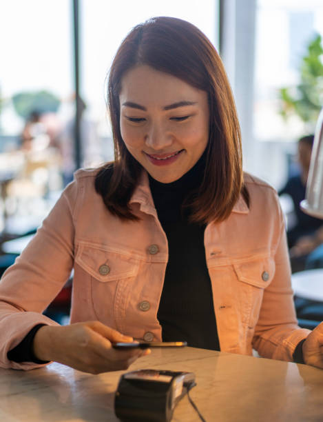 Young Asian woman making payment using mobile phone. Young Asian woman making payment using mobile phone.
Location: Singapore japan restaurant bill stock pictures, royalty-free photos & images