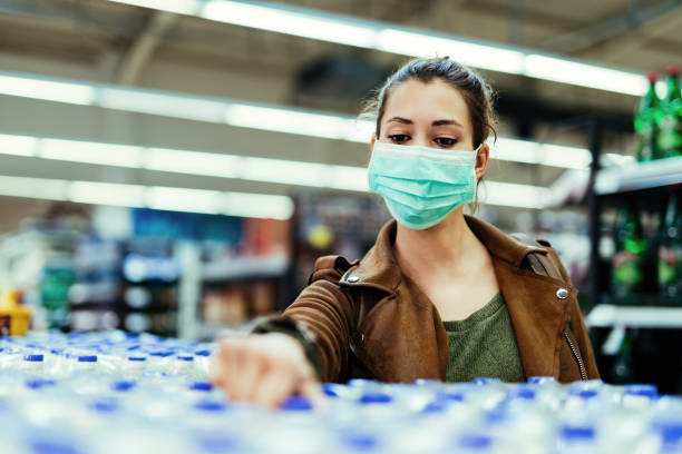 woman wearing face mask while buying bottles of water in the store during virus epidemic. - water bottle cold purified water imagens e fotografias de stock