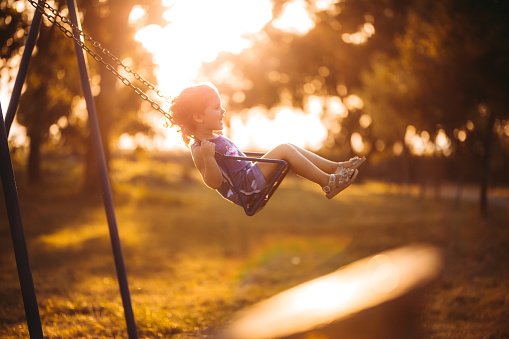 Cute little girl swinging at sunset in public park.
