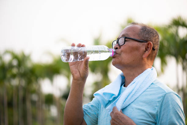 ein glücklicher alter asiatischer mann trinkt wasser im park mit sonnenlicht. gesundheits- und seniorensportkonzept. - drinking water drink men stock-fotos und bilder