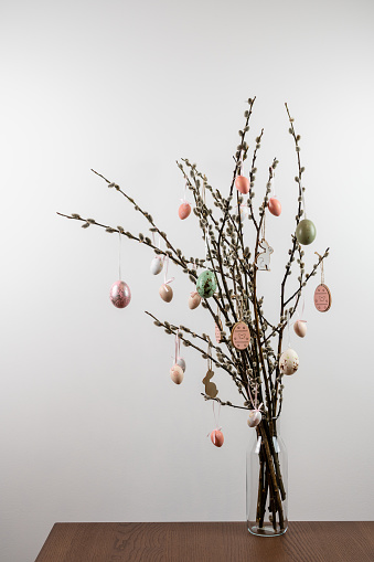 Willow tree branches in a glass vase with easter eggs hanging from the catkins