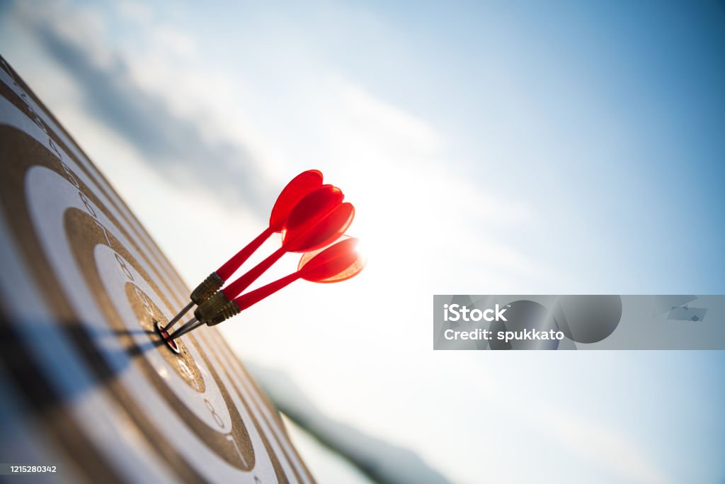 Close up shot red darts arrows in the target center on dark blue sky background. Business target or goal success and winner concept. Aspirations Stock Photo