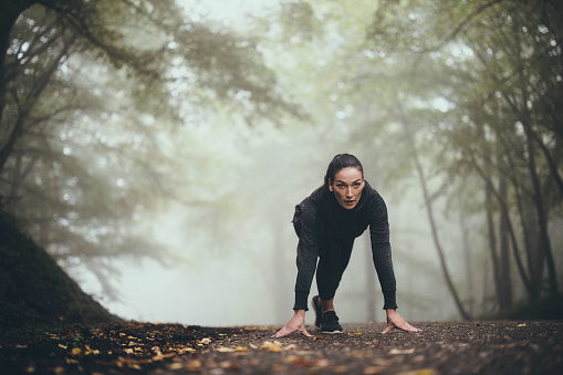 Athletic woman focusing before staring running in misty forest. Copy space.