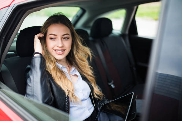 istock Smiling woman sitting in a car with tablet computer 1215292190