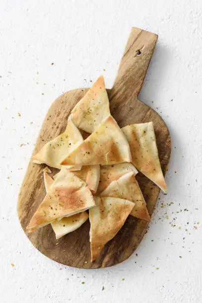 Crispy homemade pita bread chips with seasoning on a wooden cutting board