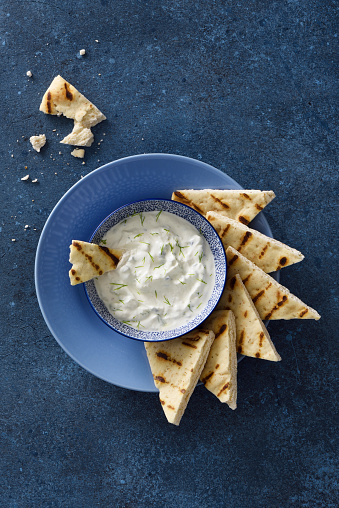 Tzatziki dip and grilled pita bread chips with seasoning on a wooden cutting board