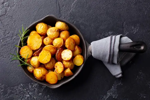 Photo of Roasted baby potatoes in iron skillet. Dark grey background. Top view.