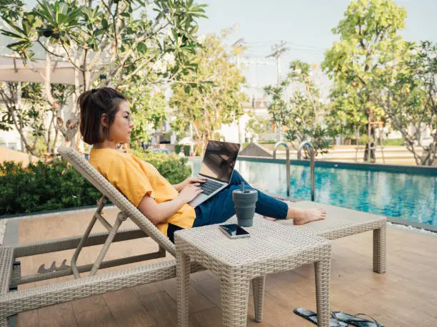 Photo of Asian women using a laptop sitting near pool in summer
