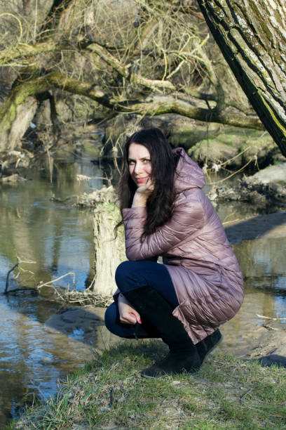 istock Girl in a spring park. Squatting by the river. 1215310524