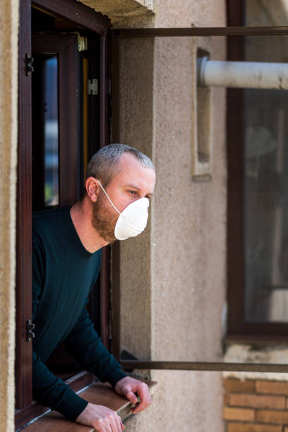 istock Man wearing protective face mask looking out window during pandemic lockdown 1215315532