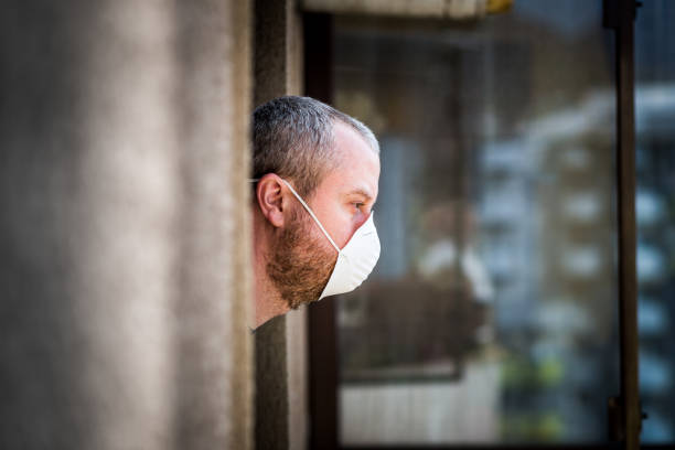 istock Man wearing protective face mask looking out window during pandemic lockdown 1215315544