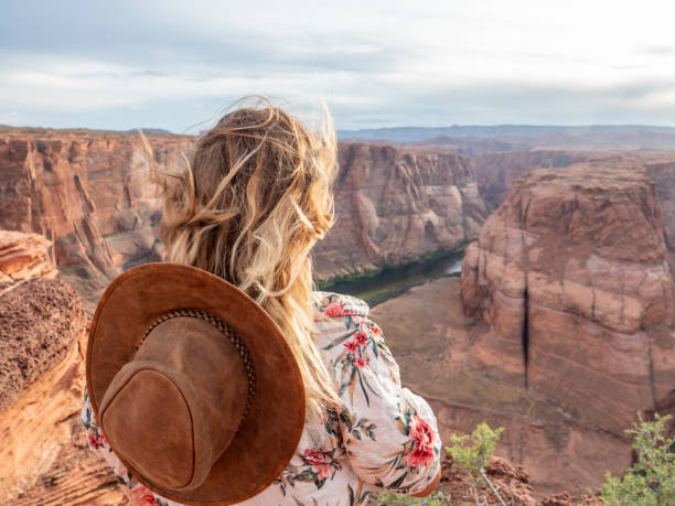 Young woman contemplating the horseshoe bend in Arizona, USA View of a girl looking at the famous horseshoe bend by the Colorado river at sunset, beautiful dramatic colourful sky. people travel concept horseshoe bend river stock pictures, royalty-free photos & images