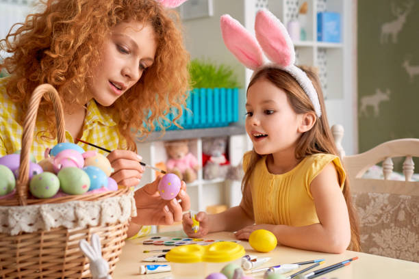 istock Easter Concept. Mother and daughter in rabbit ears sitting at kitchen coloring eggs smiling excited 1215319894