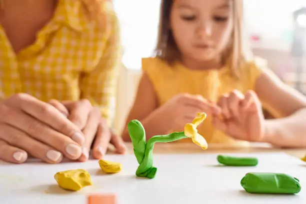 Photo of Young mother and her junior daughter playing with plasticine