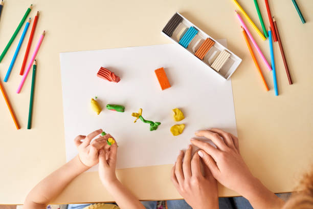 istock Home Education. Mother and daughter sitting at table molding using modeling clay top view 1215319900