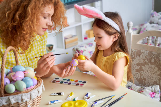 istock Easter Concept. Mother and daughter in rabbit ears sitting at kitchen coloring eggs smiling happy close-up 1215319909