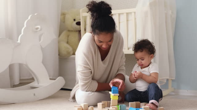 Happy african mum helping baby daughter playing wooden blocks