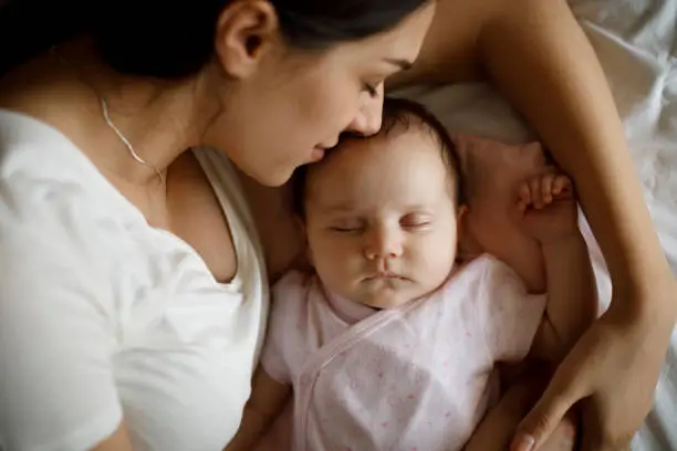 Photo of Beautiful young mother and her cute little baby sleeping in bed at home