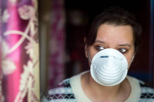 istock Woman wearing protective face mask looking out window during pandemic lockdown 1215320237