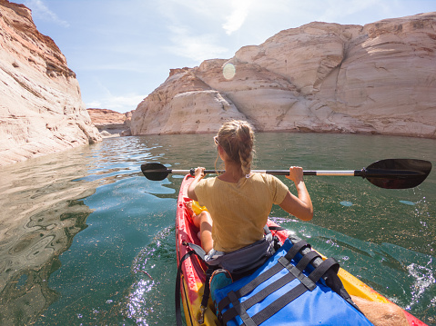 View of a young woman paddling on red canoe inside beautiful sandstone canyon in USA