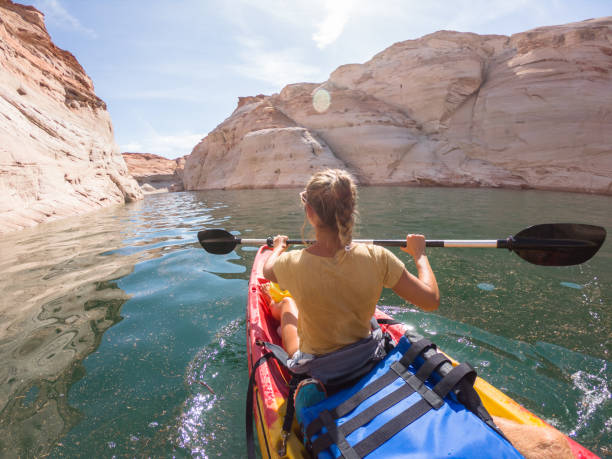 Rear view of young woman canoeing inside canyon View of a young woman paddling on red canoe inside beautiful sandstone canyon in USA page arizona stock pictures, royalty-free photos & images