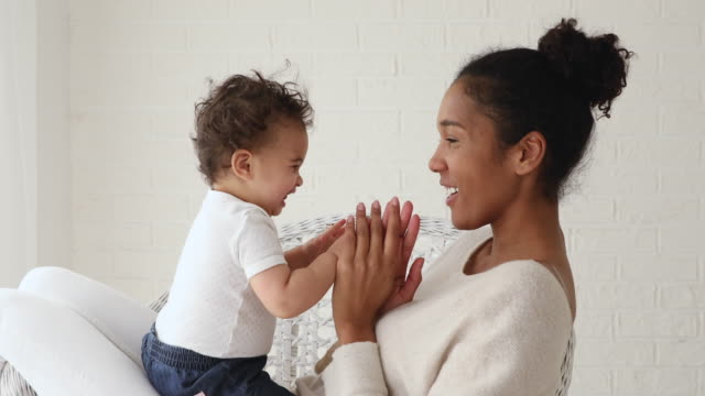 Funny infant baby playing patty cake with african mom