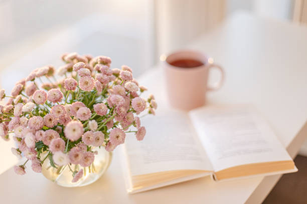 small pink flowers bouquet in glass vase with blurred soft focused book and pink cup of tea Close-up of small pink flowers bouquet in glass vase with blurred soft focused background of pink cup of tea or coffee and opened book by the window. pink tea stock pictures, royalty-free photos & images