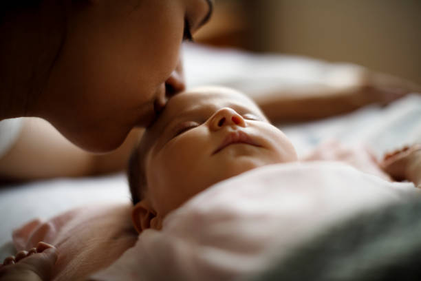 мать целует своего спящего новорожденного ребенка - baby kissing mother lifestyles стоковые фото и изображения