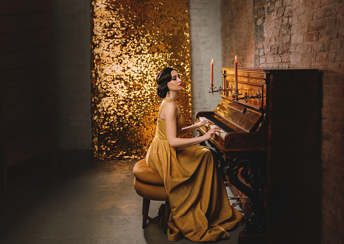 retro romantic elegant woman in golden dress play the piano. backdrop old vintage room brick wall and shine sparkle. Musician with collected bun hairstyle. vogue fashion old style 1920. Carnival party