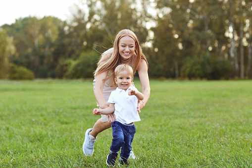 Running adorable boy with loving mother on green meadow in summer park having fun together