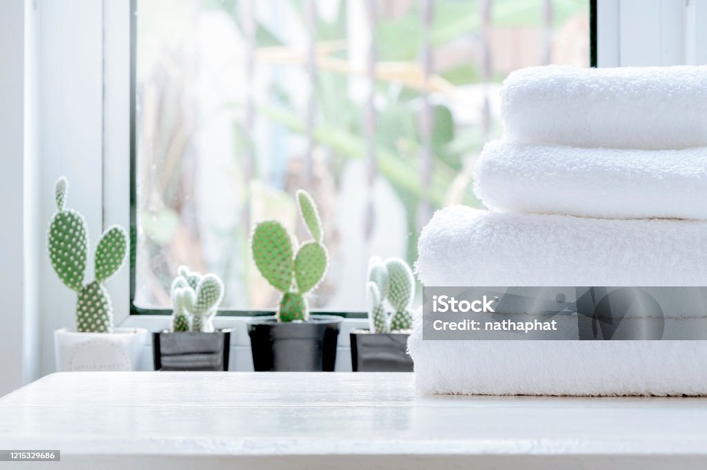 Clean towel on white table near window sill. Stack of clean towels on white wooden top table with green cactus background on window sill in modern white room. Copy space. Towel Stock Photo