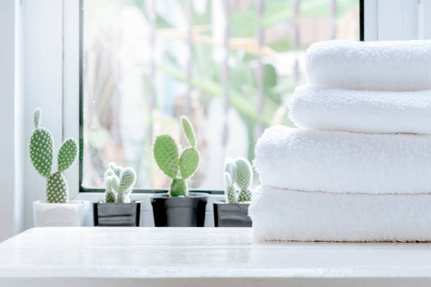 Clean towel on white table near window sill. Stack of clean towels on white wooden top table with green cactus background on window sill in modern white room. Copy space. grooming product photos stock pictures, royalty-free photos & images