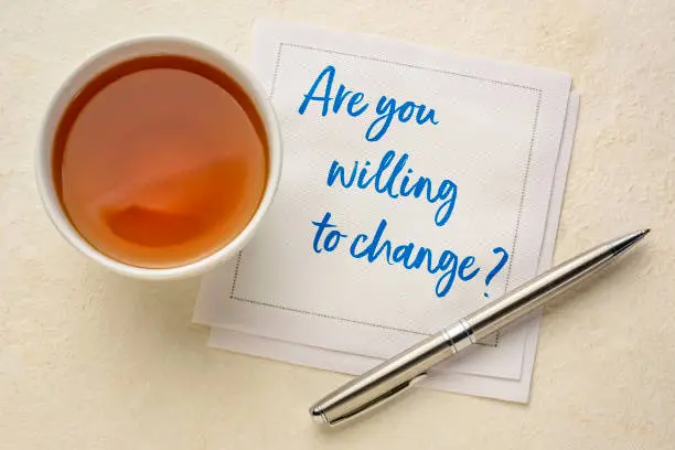 Are you willing to change? Handwriting on a napkin with a cup of tea. Self improvement and personal development concept.