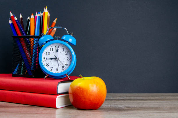 istock The blue alarm clock along with multi-colored pencils stand on a stack of red books, next to an apple 1215342138