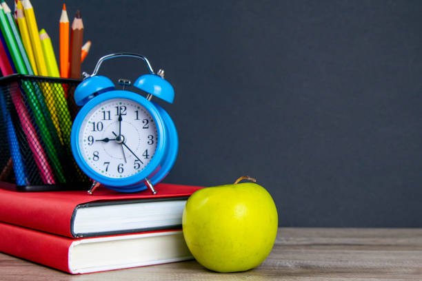 istock The blue alarm clock along with multi-colored pencils stand on a stack of red books, next to an apple 1215342152