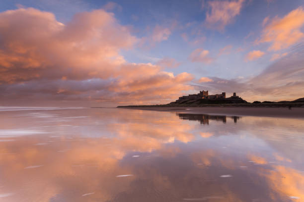 Bamburgh Castle and beach, Northumberland Bamburgh Castle and beach on the Northumberland coast at sunset with a colourful sky and cloud reflections, a popular tourist attraction and beautiful location in North East England. Bamburgh stock pictures, royalty-free photos & images