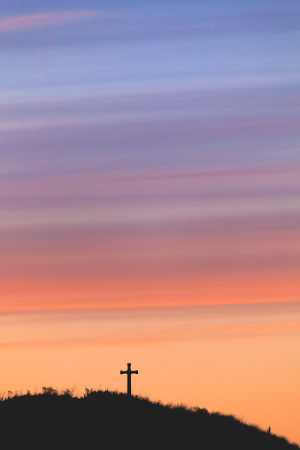 Silhouette of St Cuthberts Cross on the brow of a hill overlooking Alnmouth on the Northumberland coast at sunset with a vivid pink and red sky.