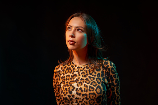 Close-up portrait of a woman in leopard print clothing looking up at blank copy space, on dark background with colorful backlight