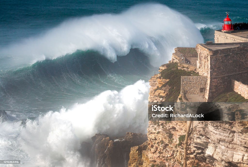 Biggest Wave In The World, Nazare, Portugal Stunning Image of giant wave crashing into cliff and lighthouse  after major Atantic Storm. Nazare Stock Photo