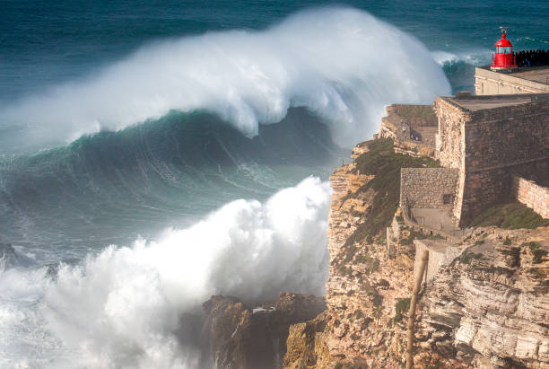 Biggest Wave In The World, Nazare, Portugal Stunning Image of giant wave crashing into cliff and lighthouse  after major Atantic Storm. nazare surf stock pictures, royalty-free photos & images